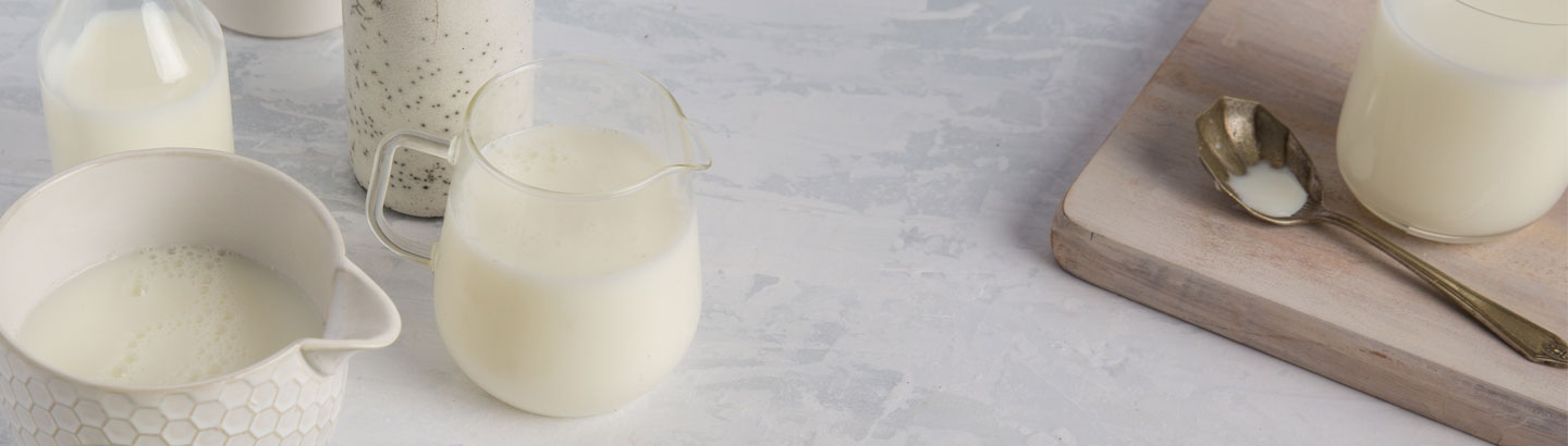 A picture of different types of milk products in glasses on a bench.